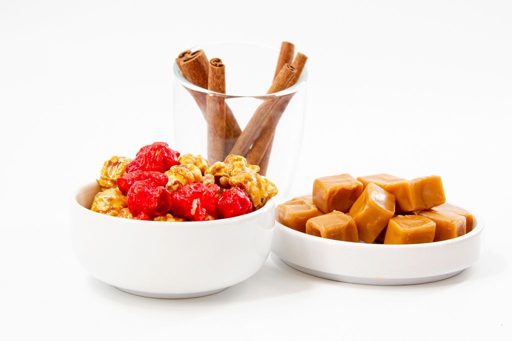 Redhots Cinnamon Popcorn, the best Caramel Corn, displayed in white bowl with caramel chews and cinnamon sticks