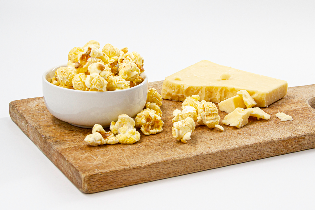 decadent white cheddar popcorn in white bowl with creamy cheese displayed on wood cutting board