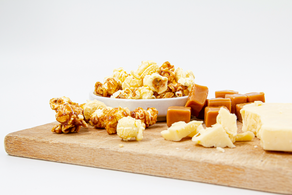 Caramel and White Cheddar Popcorn displayed on wood cutting board with real white cheddar cheese chunks and softy, chewy caramel candy.