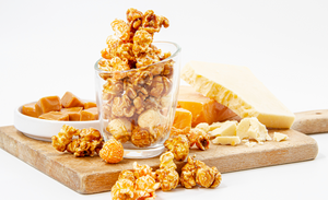 C3 - Tasty Cheese, White Cheddar & Caramel Popcorn displayed on cutting board with gourmet popcorn, caramel candy and cheddar cheese cubes