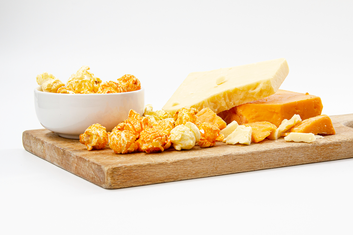 Savory Cheese Corn and White Cheddar Popcorn displayed on wood cutting board with cheddar cheese and white cheddar cheese chunks.