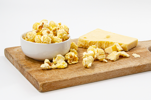 white cheddar popcorn in white bowl with cheese displayed on wood cutting board